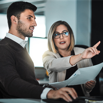 two people holding paper, one pointing at screen