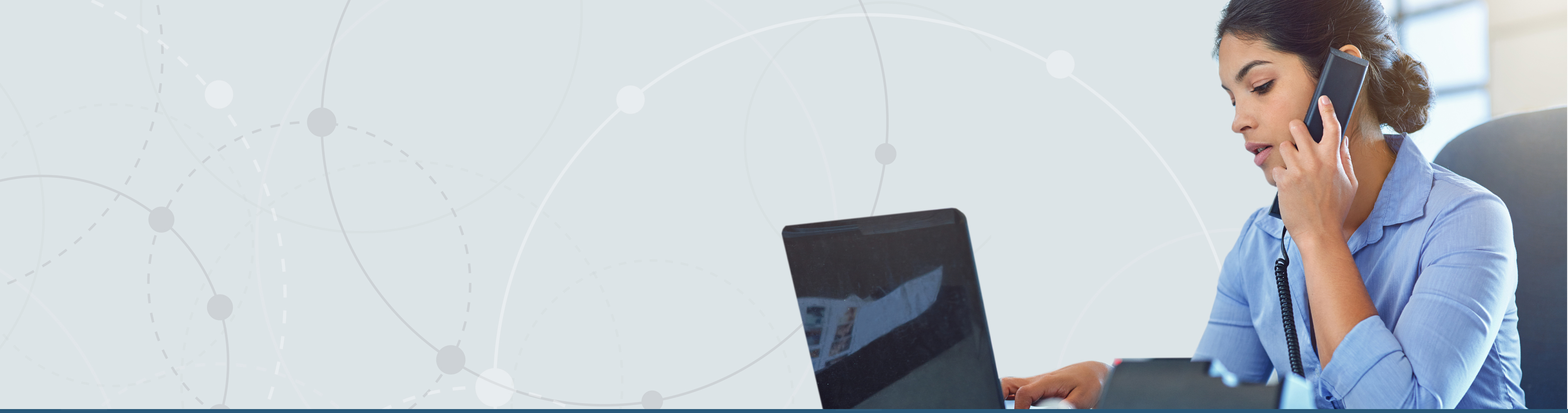 person viewing laptop and holding mobile phone to ear